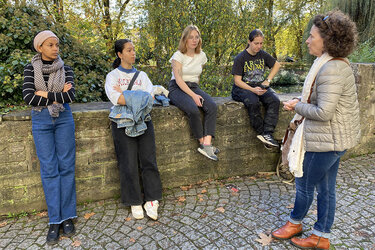 Gaststudierende sitzen auf eine Mauer in Tübingen höhren der Stadtführerin zu.