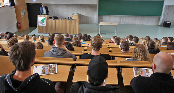 Studierende sitzen in der Aula und schauen auf die Bühne zum Dozenten.