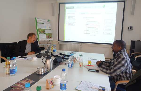 Jannis Bahnmüller zusammen mit Pierre Maniragarura an einem Besprechungstisch beim Besuch der Partnerorganisation AgrarKontakte International (AKI) e.V. an der HFR