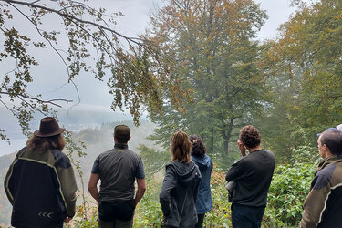 Studierende blicken aus dem Wald in die Landschaft