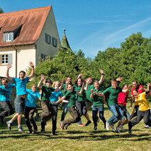 Studierende springen vor der Hochschule in die Luft und lachen