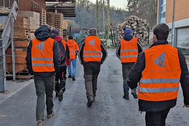 Studierende laufen mit orangenen Warnwesten über das Sägewerksgelände.