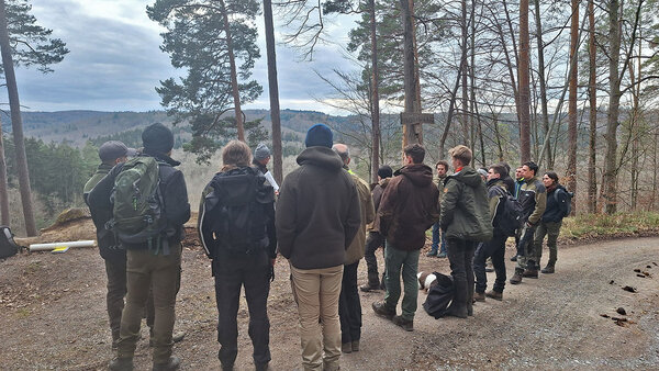 Studierende stehen vor Prof. Schurr im Wald und hören diesem zu