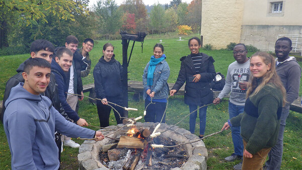 Gaststudierende und deren Buddys stehen grillend an der Grillstelle im Arboretum der Hochschule und lächeln in die Kamera.