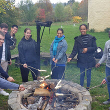 Gaststudierende und deren Buddys stehen grillend an der Grillstelle im Arboretum der Hochschule und lächeln in die Kamera.