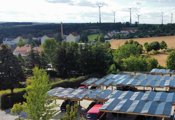 Photovoltaik auf Parkplatzüberdachung. Im Hintergrund Windräder.