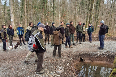 Studierende stehen um ein mit Wasser gefülltes Bodenloch und lassen sich diese von Prof. Schurr erläutern