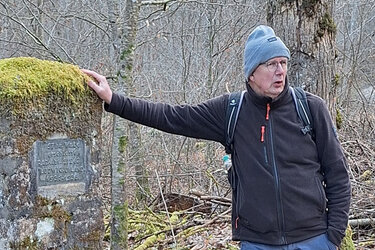 Prof. Schurr steht an einem Gedenkstein im Wald und referiert