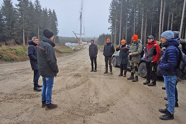 Studierende stehen auf der Baustelle und hören dem Referenten zu. Dr. Matthais Pavel erläutert der Rottenburger Exkursionsgruppe Planung und Bau der Hoßkircher Windräder. 