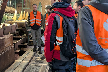 Studierende stehen mit orangenen Warnwesten im Sägewerk und betrachten die Sägewerkstechnik.